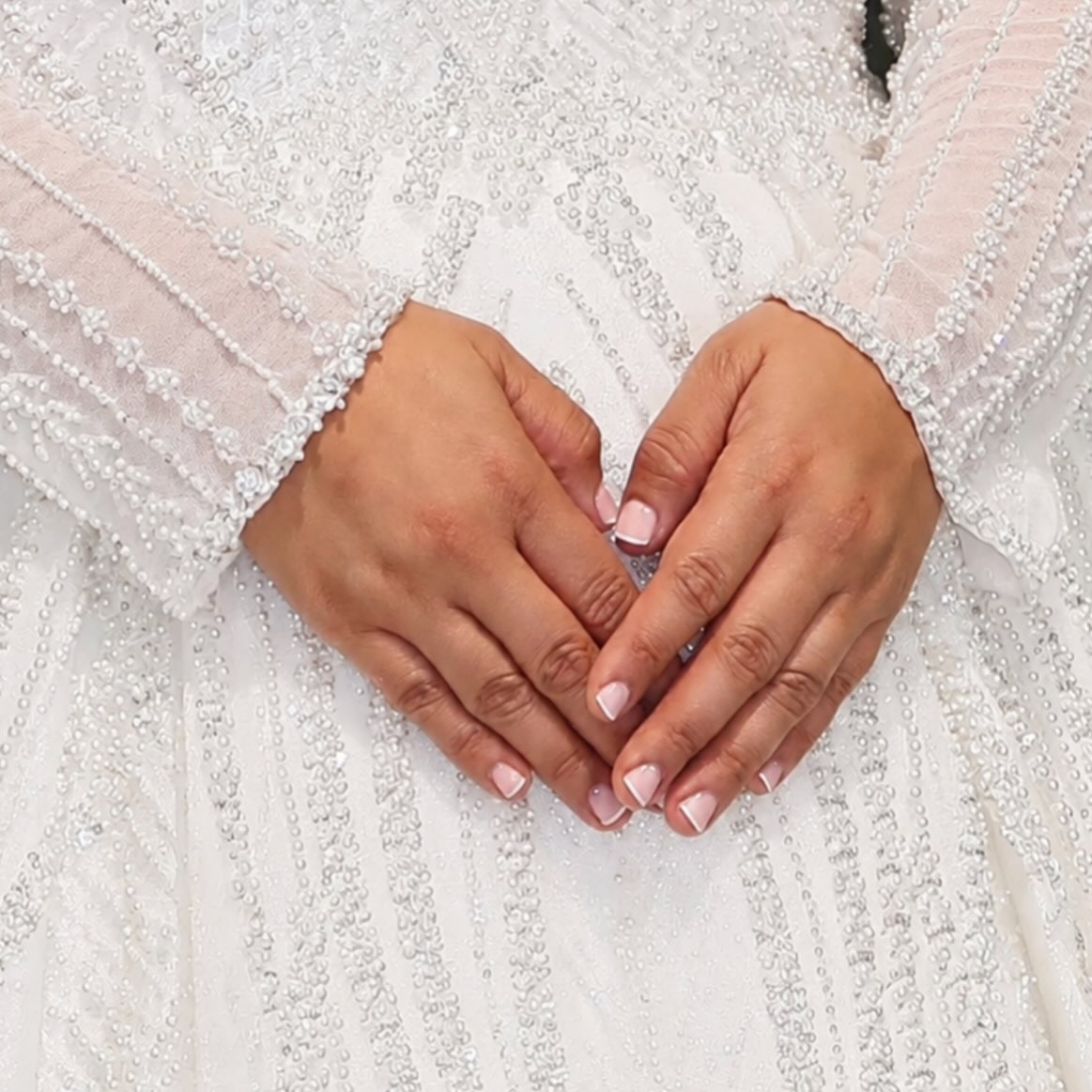 French manicure op twee handen tegen een jurk met parels en kraaltjes